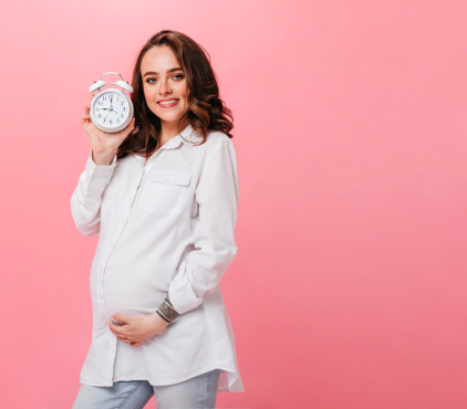 Smiling pregnant woman holding a clock, symbolizing due date awareness and timely prenatal care – Rainbow Children's Hospital